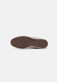 Canvas sneaker sole with a geometric tread pattern, brown rubber material, white midsole, and red accents near the upper edges.
