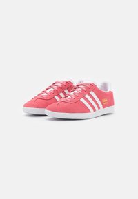 Pink suede sneakers featuring white stripes and branding, with a classic low-top design and textured surface. White rubber sole.