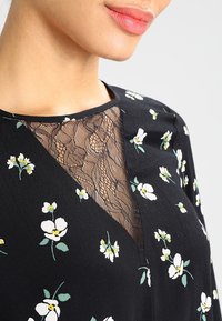 Abito nero con un motivo floreale, caratterizzato da un'inserto in pizzo sul colletto. Le maniche corte e il tessuto leggero conferiscono un aspetto fluttuante.