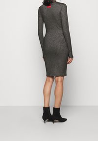 Abito a maniche lunghe, aderente in maglia a costine metallizzata nera, con collo alto e spacchi laterali, abbinato a stivali neri al polpaccio.