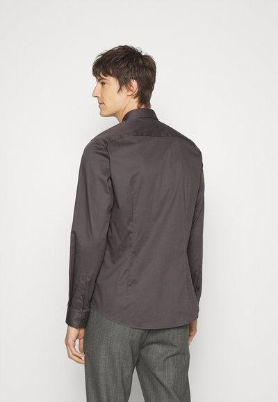 Camisa cinza escura com botões, de mangas longas, colarinho estruturado, textura suave e brilho sutil, combinada com calças cinza com padrão.
