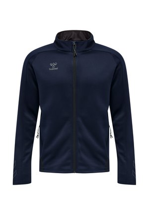 Marineblaue Zip-up-Jacke mit Stehkragen, seitlichen Reißverschlusstaschen, dezentem Hummel-Logo auf der Brust und reflektierenden Chevron-Mustern auf den Ärmeln.