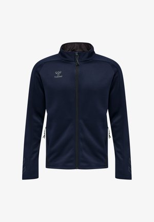 Marineblaue Zip-up-Jacke mit Stehkragen, seitlichen Reißverschlusstaschen, dezentem Hummel-Logo auf der Brust und reflektierenden Chevron-Mustern auf den Ärmeln.