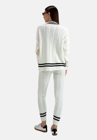 Witte kabelgebreide trui en bijpassende broek, met zwarte strepen bij de manchetten en de zoom. Afgewerkt met een textuurpatroon en casual sneakers.
