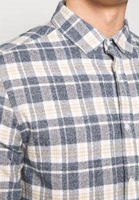 Karierte Hemd in Grau, Weiß und Gelb; durchgeknöpfter Kragen; strukturierter Stoff; markantes Karomuster mit feinen Linien.