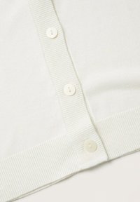 Nahaufnahme eines weißen Strickcardigans mit gerippten Kanten und drei runden weißen Knöpfen entlang der vorderen Knopfleiste.