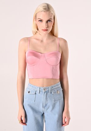 Top corto rosa realizzato in tessuto morbido con spalline sottili, dotato di cuciture curvate sul busto e una leggera lucentezza, abbinato a jeans azzurri a vita alta.
