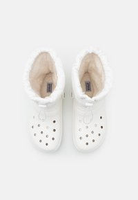 Botas brancas impermeáveis com um interior suave forrado a pelo, apresentando um formato arredondado, cordão ajustável no tornozelo e orifícios de ventilação circulares.