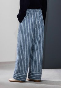 Niebiesko-białe szerokie spodnie w paski z teksturowanej tkaniny, z marszczoną talią i ozdobnym paskiem na dole.