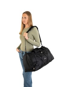 Black duffel bag with a solid texture, featuring a zip closure, dual handles, and adjustable shoulder strap. Includes decorative elastic accents.