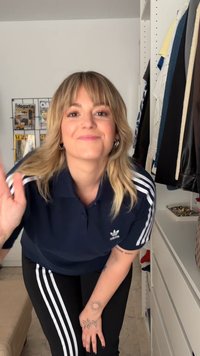 Navy polo shirt with white Adidas logo, paired with black pants featuring three white stripes. Smooth fabric textures and casual fit.