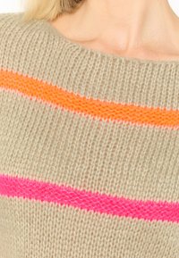 Beige gebreide trui met drie horizontale strepen: één neonoranje en twee felroze. De textuur lijkt zacht, met een ontwerp van een brede halsopening.