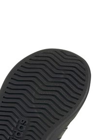 Semelle de chaussure en caoutchouc noir avec motif de bande de roulement ondulé et logo "adidas" en relief près du talon, sur fond blanc.