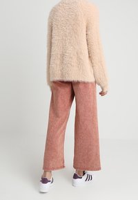 Fluffy beige sweater, loose pink wide-leg pants, and white sneakers with purple accents. Soft texture, relaxed fit, casual outfit.