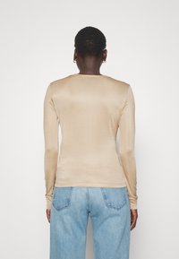 Langärmliges, beiges Oberteil aus einem glatten, enganliegenden Stoff. Verfügt über einen runden Ausschnitt und ein einfaches Design, kombiniert mit hellblauen Jeans.
