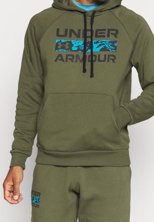 Oliwkowa zielona bluza z kapturem z czarnym napisem "UNDER ARMOUR" oraz niebieskim kamuflażowym akcentem. Posiada kieszeń typu kangur i kaptur ze sznurkiem. Wykonana z bawełnianej mieszanki tkaniny.