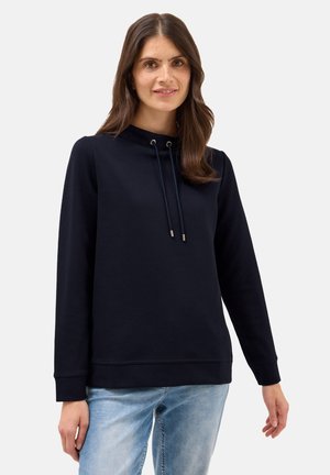 Sweatshirt bleu marine avec un col montant, cordon de serrage, manches longues, poignets côtelés et une texture douce, associé à un jean délavé.