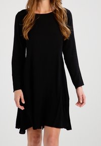 Svart långärmad klänning med rund halsringning, flödande A-linjeform och mjuk tygtextur, med sidofickor för funktionalitet.