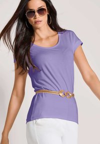 Lavendel kortgebloemde top met een ronde halslijn, gecombineerd met een gouden riem met cirkelvormige accenten, gedragen met witte broek.