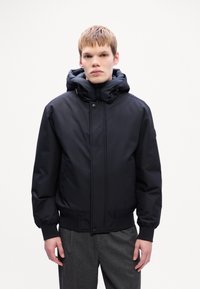 Veste rembourrée noire avec un col haut et une capuche réglable. Équipée d'une fermeture éclair à l'avant et d'une fermeture à pression, de poignets côtelés et d'une texture lisse.