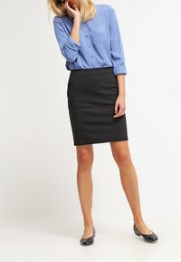 Camisa de botón azul claro con mangas arremangadas, combinada con una falda lápiz negra y zapatos planos negros. Tela suave y diseño ajustado.