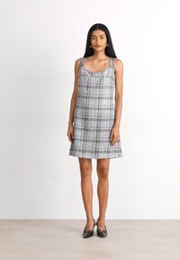 Harmaa ruudullinen mekko yksinkertaisella hihattomalla suunnittelulla, jossa on pyöreä pääntie, jota koristavat paljetit ja liehuva siluetti.