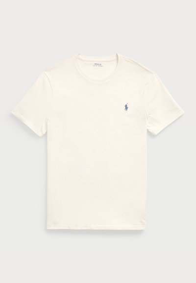 Kremna bombažna majica s kratkimi rokavi in okroglo ovratnikom. Ima majhen modro vezen logotip na levem prsnem delu.