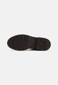 Semelle de botte en caoutchouc noir avec grip texturé. Présente des stries et un motif en étoile, conçue pour l'adhérence. Construction plate et robuste.