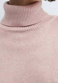 Hellsrosa Rollkragenpullover aus geripptem Strickstoff, mit hohem Kragen und strukturiertem Muster.