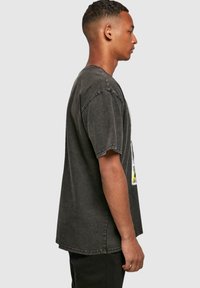 Camiseta negra de gran tamaño con mangas cortas, textura desgastada y estampado gráfico. La vista lateral muestra un ajuste relajado y costuras de hombro caídas.