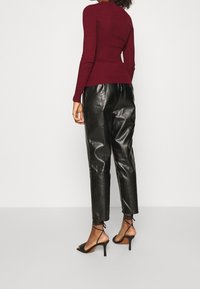 Top a maniche lunghe rigate color bordeaux abbinato a pantaloni in pelle nera a gamba affusolata e tacchi alti neri con cinghie. Presenta una silhouette aderente e una texture morbida.