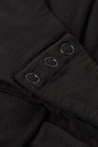 Svart tyg med en mjuk, texturerad yta, med tre runda svarta knappar längs kanten. Inga ytterligare mönster eller beslag syns.