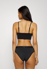 Zwarte naadloze bralette met verstelbare banden en bijpassende high-waisted briefs. Gladde stof met een subtiele textuur en logo-detail op de tailleband.