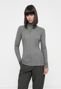 Siva turtleneck majica od mekanog, teksturiranog materijala, uskog kroja i dugih rukava, u kombinaciji s tamnosivim hlačama visokog struka.