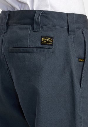 Pantalones RVCA de color gris oscuro con una tela texturizada, múltiples bolsillos y parches de logotipo en negro y amarillo en la parte posterior y lateral.