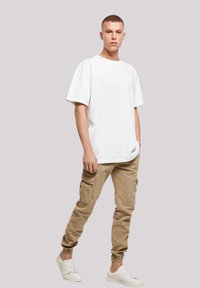 White cotton oversized t-shirt, beige cargo pants with side pockets, and white sneakers. Simple and casual design with a relaxed fit.