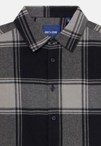Zoom na črno-sivo karirano srajco s kratkimi rokavi in ovratnikom, z nalepko "ONLY & SONS" v notranjosti ovratnika.