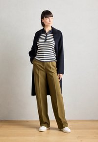 Haut à manches longues rayé, manteau bleu marine, pantalon large vert olive, baskets blanches ; mettez l'accent sur la texture et les couleurs contrastées.