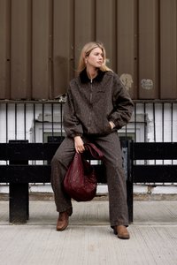 Løveprint, brun stoffjakke og bukser, svart krage, stylet med en bordaux-veske med grommetdetaljer, og brune ankelboots.