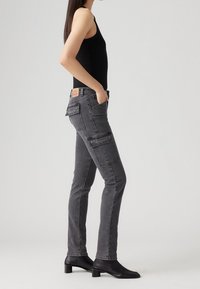 Vaqueros de denim gris de corte ajustado con dos bolsillos tipo cargo, una textura sutil y una etiqueta de marca en la parte trasera de la cintura. Combinados con una parte superior negra y tacones.