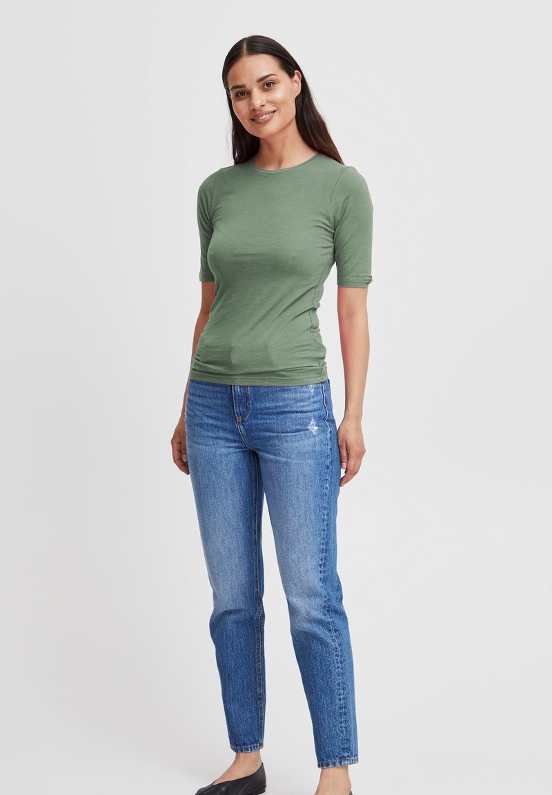 Green short-sleeve t-shirt with a crew neck, paired with light blue straight-leg jeans. The fabric appears smooth and fitted.