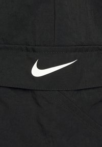 Svart tyg med en texturerad yta, med en vit Nike swoosh-logotyp. Designen inkluderar synliga sömmar och vinklade sömmar.