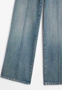Light blue denim jeans with a loose fit, featuring front pleats, straight legs, and visible stitching along the edges.