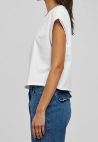Top bianco in cotone a maniche corte con vestibilità rilassata e risvolti, abbinato a jeans in denim blu a vita alta con taglio classico.