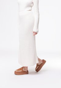 Abito a costine di colore bianco sporco, con maniche lunghe e silhouette aderente, abbinato a sandali a piattaforma marroni con fodera in pelliccia.