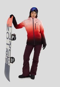 Gevoerde, gradient jas in roze naar zwart, gedragen met donkerpaarse broek. Zwarte handschoenen, skibril en een snowboard met witte graphics.