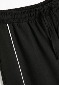 Sorte atletiske shorts med elastisk talje, snor og hvid stribe på siden. Fremstillet af blødt, strækbart materiale med en glat tekstur.