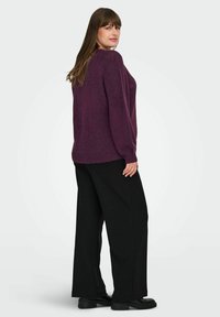Violet mezgimas megztinis su tekstūruotu pečių detalėmis, derinamas su juodomis plačiomis kelnėmis ir juodais platforminiais batais. Neutralus fonas.