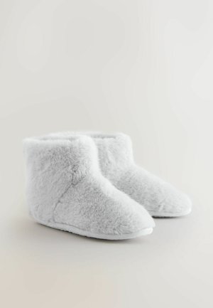 Harmaat tekoturkiskorsettilyhyet saappaat, joissa on pehmeä tekstuuri, pyöreä kärki ja valkoinen kumipohja. Muotoilu on yksinkertainen ja kodikas.