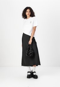 T-shirt blanc avec un petit motif, jupe en satin noire, sac fleuri noir, chaussettes blanches et chaussures compensées noires. Cheveux bouclés.